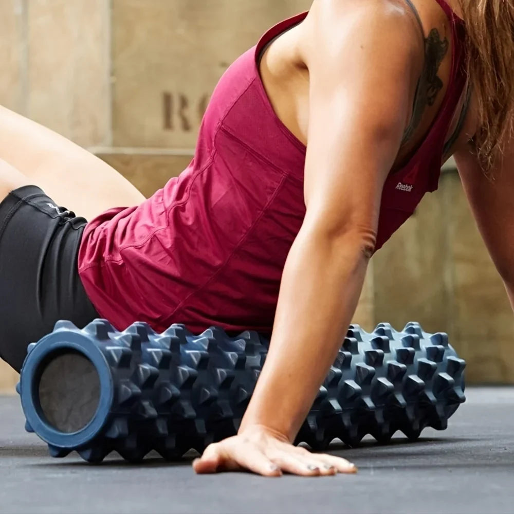 Woman using black Wolf Tooth Yoga Foam Roller for muscle relaxation on gym floor
